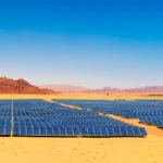 Expansive solar farm with rows of blue solar panels in a desert under a clear blue sky.