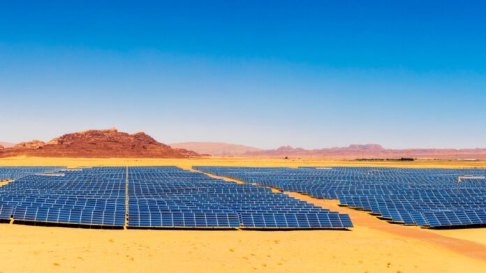 Expansive solar farm with rows of blue solar panels in a desert under a clear blue sky.