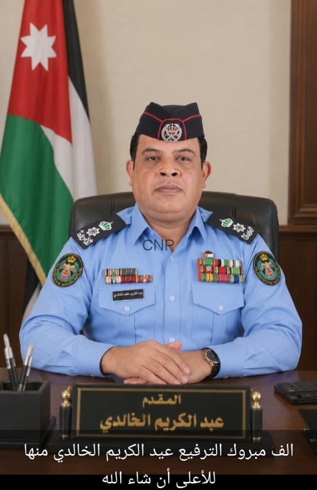 sabd - Center News Network Portrait of a Jordanian police officer in a blue uniform with medals, seated at a desk with a Jordanian flag in the background.