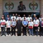 Group of uniformed officers and officials posing for a ceremony photo outside a building with emblems above the entrance.