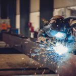 Welder in protective gear arc-welding a steel beam in a workshop, sparks flying around the bright arc.