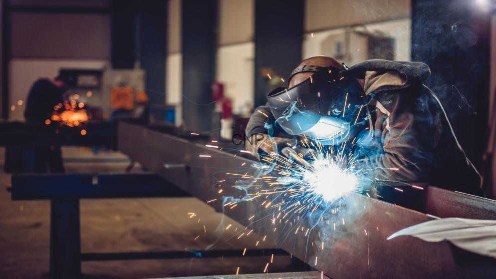 Welder in protective gear arc-welding a steel beam in a workshop, sparks flying around the bright arc.