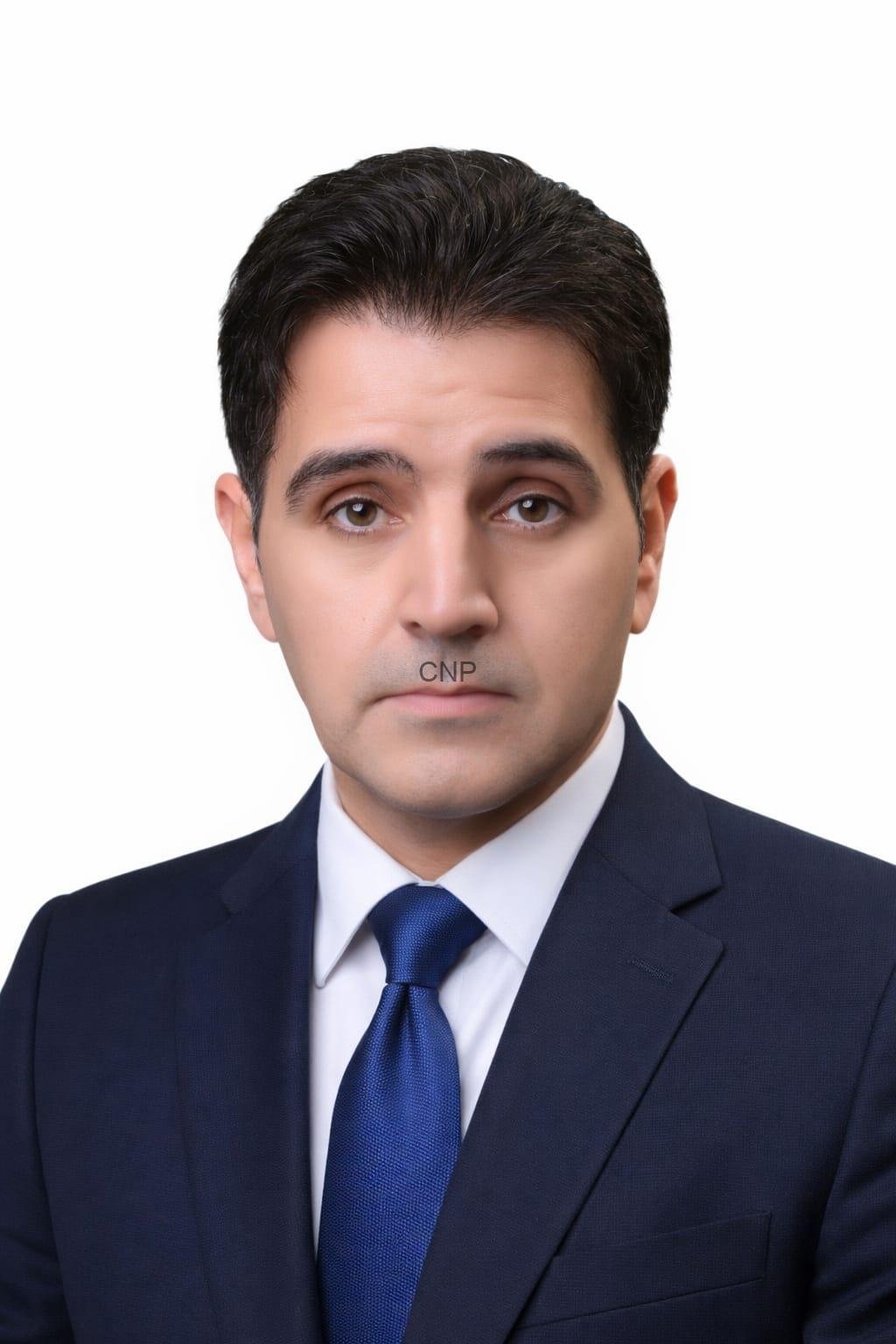 Professional head-and-shoulders portrait of a man in a navy suit and blue tie with neutral expression, white background.
