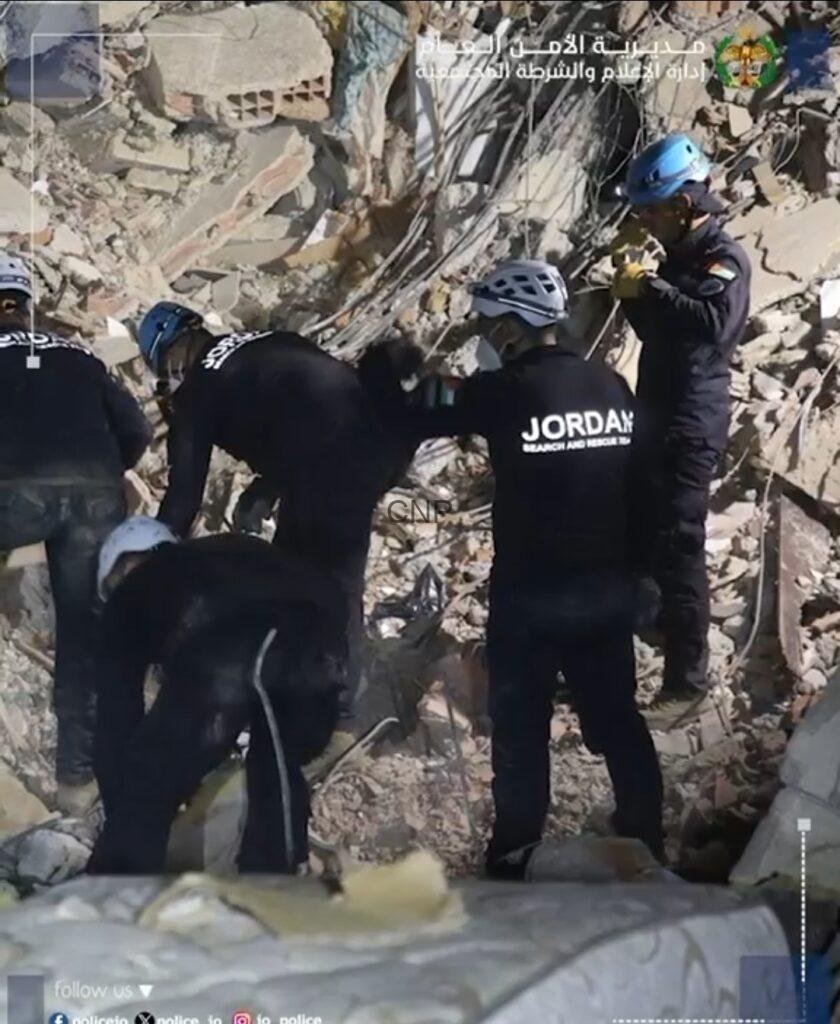ss7 - Center News Network Rescue workers in black uniforms and helmets search debris in a collapsed building, one labeled Jordan Search and Rescue, amid tangled rebar and rubble