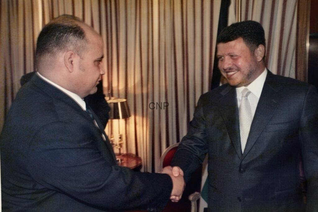 ssddss - Center News Network Two men in dark suits shaking hands in an indoor setting, smiling as they greet each other.