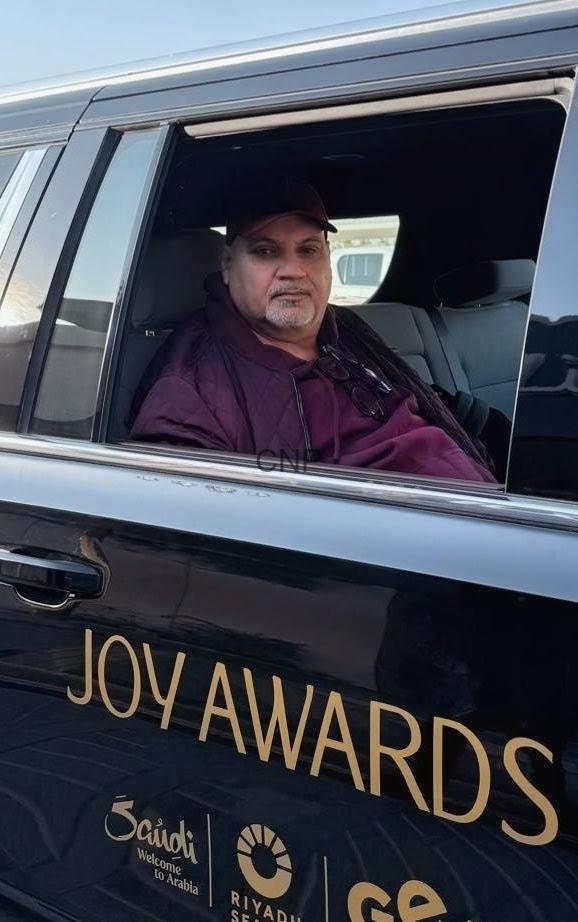 sss15 - Center News Network Man in a maroon jacket sits in a black car window beside 'JOY AWARDS' on the vehicle's exterior.