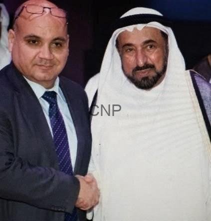 sss444 - Center News Network Two men in formal attire shaking hands: one in a suit and tie, the other in a white traditional thawb and head covering, both smiling slightly.