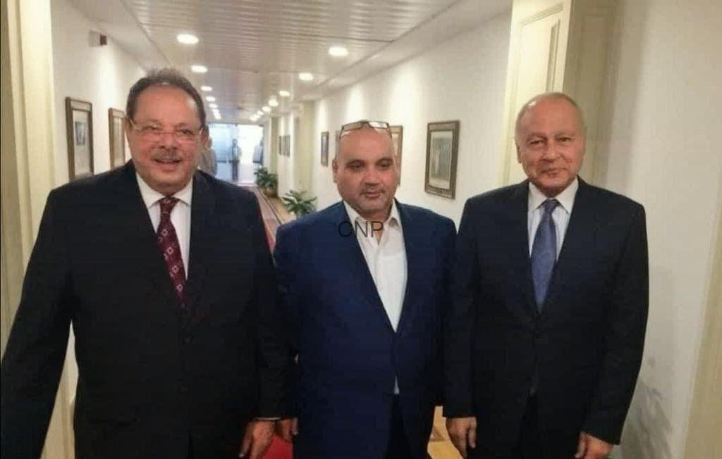 sss888 - Center News Network Three men in business suits walk down a well-lit hallway, posing for a photo in a formal setting.