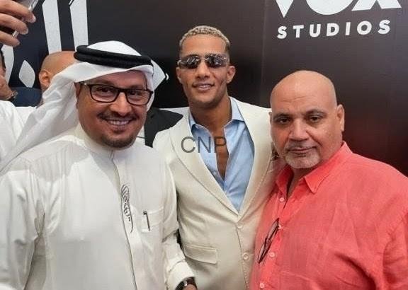 ssss22 - Center News Network Three men pose for a photo at a Vox Studios event: left in white traditional attire and glasses, middle in a beige blazer with sunglasses, right in a coral shirt.