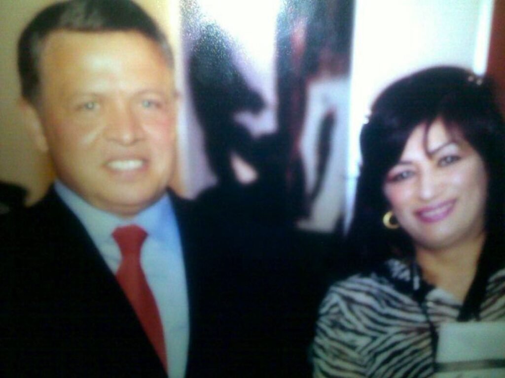 Two adults posing for a photo, smiling at the camera, man in a suit with a red tie and woman with striped top on the right.