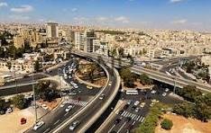 Aerial view of a complex multi-level highway interchange weaving through a dense urban area with beige buildings under a blue sky.
