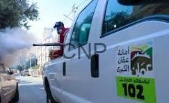 White emergency vehicle with Arabic text and 102, a firefighter stands on its rear step as smoke billows nearby.