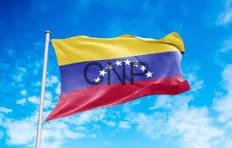 Venezuelan flag waving on a flagpole against a bright blue sky.