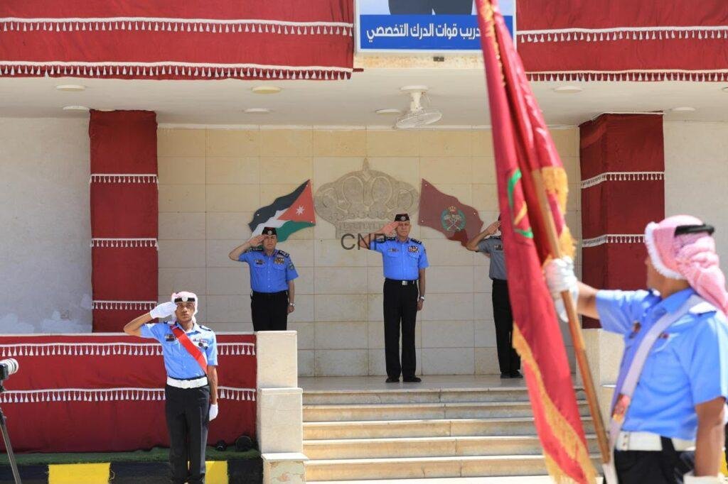 haf2 - Center News Network Three air force officers salute on a tiled stage during a ceremony, with a flag bearer in the foreground and a national flag in the background.
