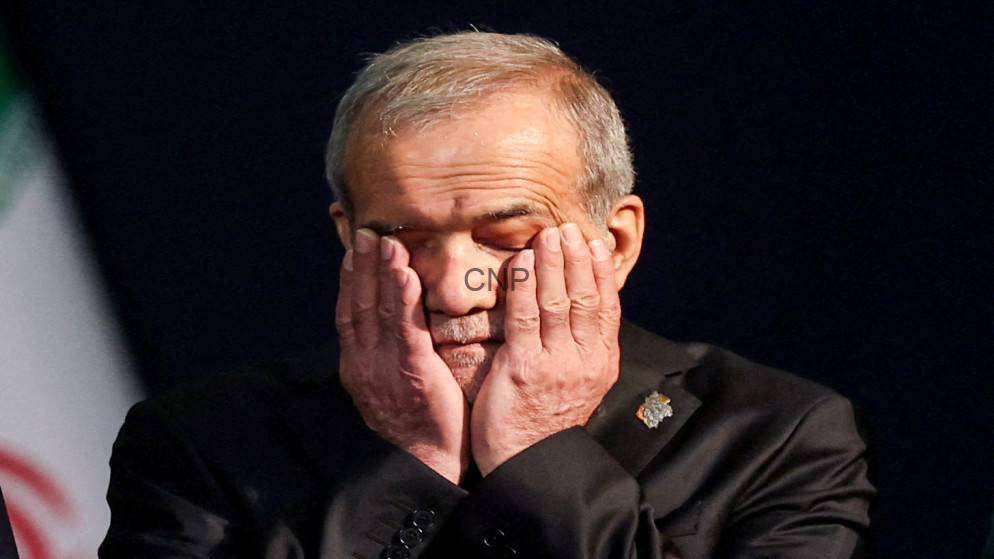 Older man with gray hair holding his face in his hands on a dark stage, eyes closed in thought or fatigue.