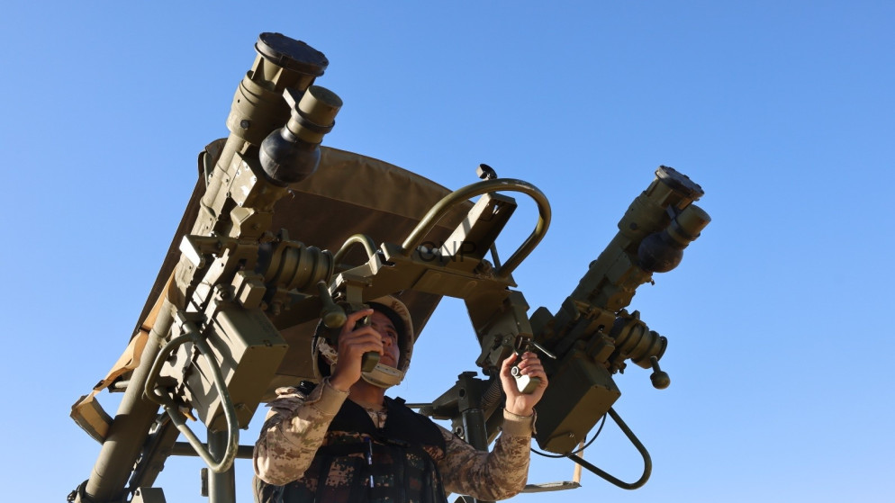 image - Center News Network Military service member in desert camouflage operating a large dual-barrel mounted weapons system outdoors under a blue sky
