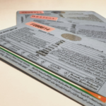 Three overlapping driver’s license cards with multilingual text and vehicle information on a light surface.