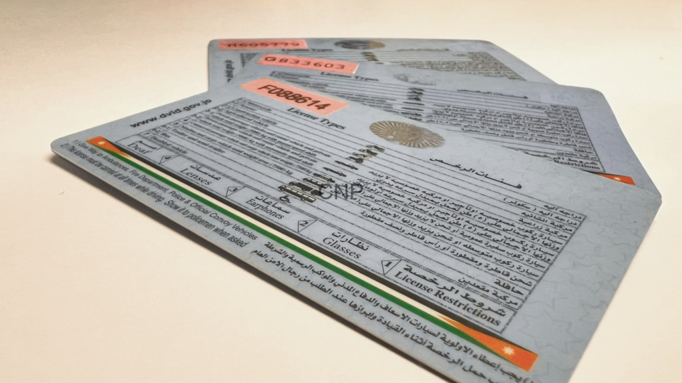 image - Center News Network Three overlapping driver’s license cards with multilingual text and vehicle information on a light surface.