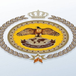 Official emblem with an eagle perched over a globe/map motif, surrounded by a gold laurel wreath and crown, on a yellow circular background with a banner.
