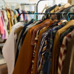 Clothes on racks in a shop, assorted coats and shirts on wooden hangers in a clothing store setting.