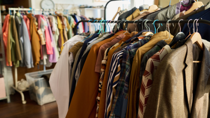 Clothes on racks in a shop, assorted coats and shirts on wooden hangers in a clothing store setting.
