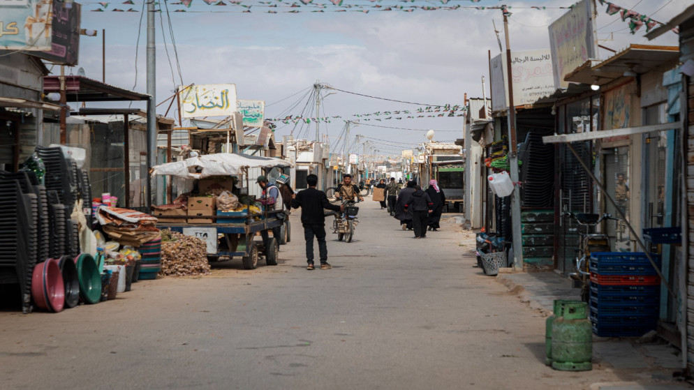 image - Center News Network Busy market street in a Middle Eastern town with stalls, vendors, and shoppers along a paved road under string bunting.
