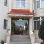 Beige stone building entrance with red-tiled awning, glass doors labeled 'CNR', concrete steps, and potted plants on either side.
