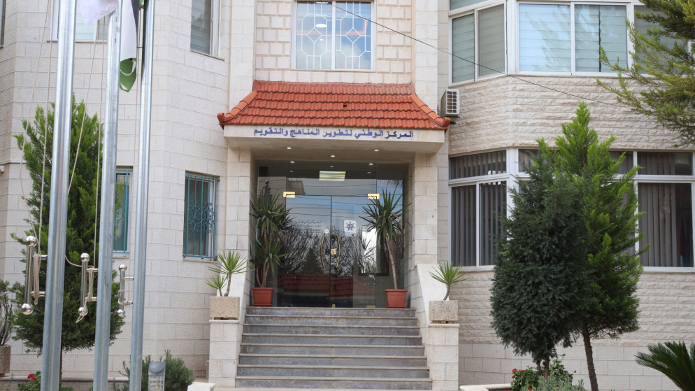 Beige stone building entrance with red-tiled awning, glass doors labeled 'CNR', concrete steps, and potted plants on either side.