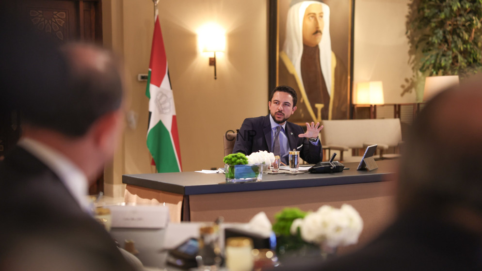 image - Center News Network Jordanian official speaks at a formal meeting table with the flag and portrait in the background, attendees blurred in foreground