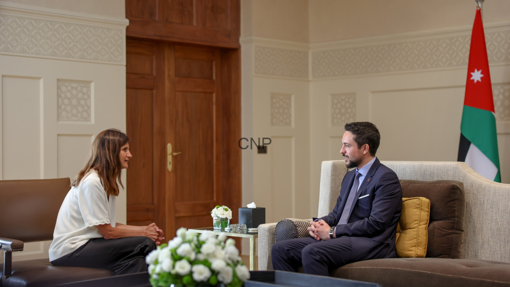 image - Center News Network Two people sit facing each other in a formal office: a woman in a white blouse and a man in a navy suit, with a Jordanian flag in the background.