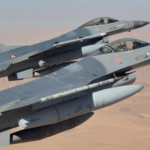 Two gray fighter jets in tight formation flying over a desert landscape, Jordanian flag insignia on the tails visible.
