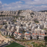 A densely packed hillside neighborhood of beige apartment blocks cascading across terraced slopes under a blue sky