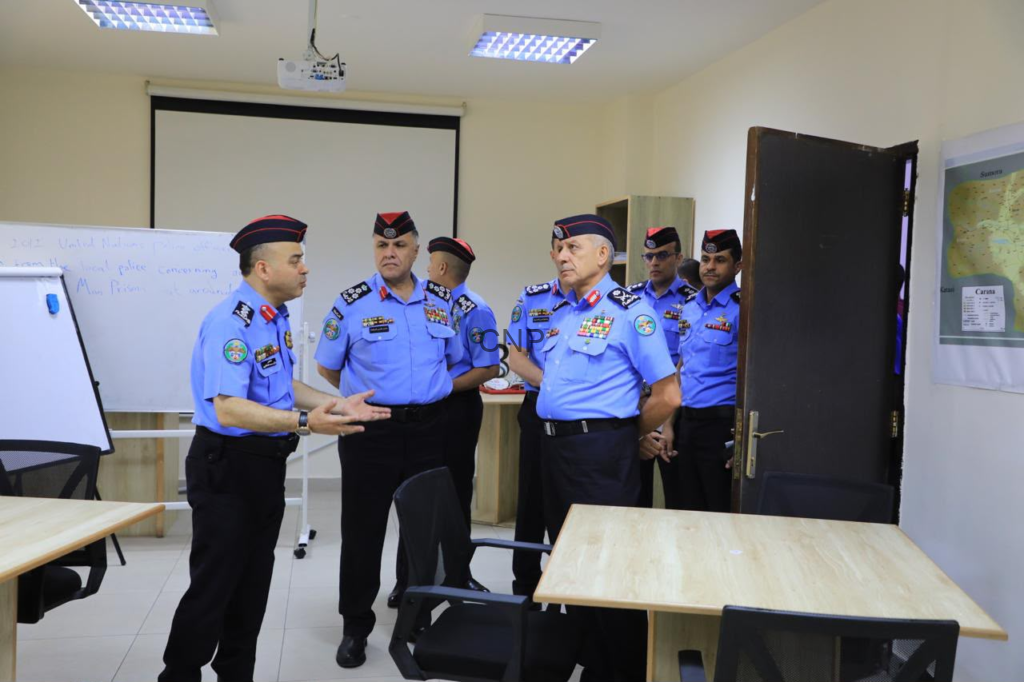 Group of police officers in blue uniforms and red berets standing in a classroom, one officer speaking as others listen.