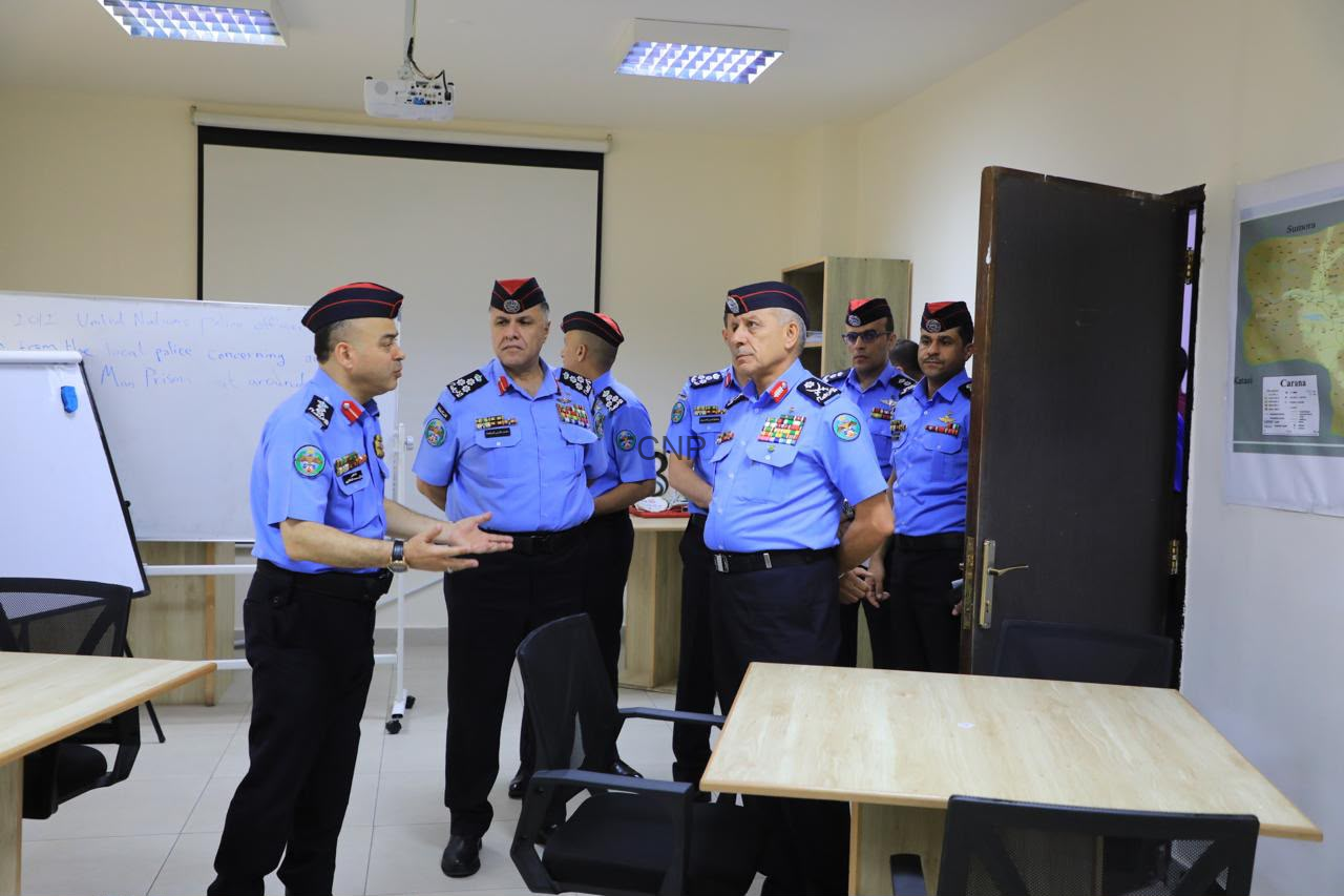 Group of police officers in blue uniforms and red berets standing in a classroom, one officer speaking as others listen.