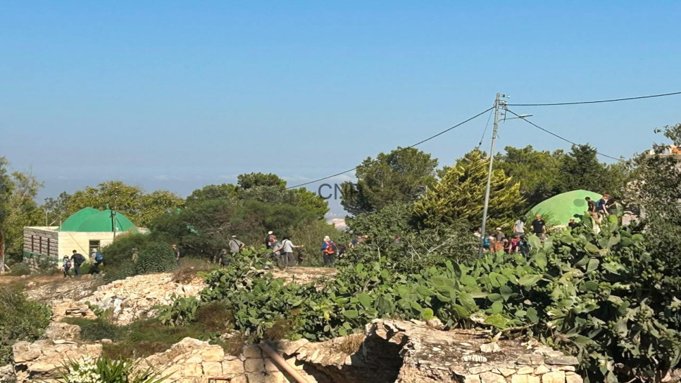 image - Center News Network Group of hikers near bright green dome tents on a rocky hillside with cactus and stone walls under a clear blue sky.