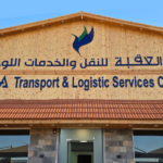 Facade of a wooden building with a blue logo and bilingual sign reading 'AQABA Transport & Logistic Services Company' (Arabic text above).