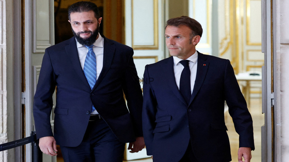 Two men in dark suits walk out of an ornate doorway, one wearing a blue striped tie, the other with a black tie, looking ahead.