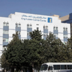 White King Hussein Cancer Center building with blue accents, trees in front, and a bus on the street nearby.
