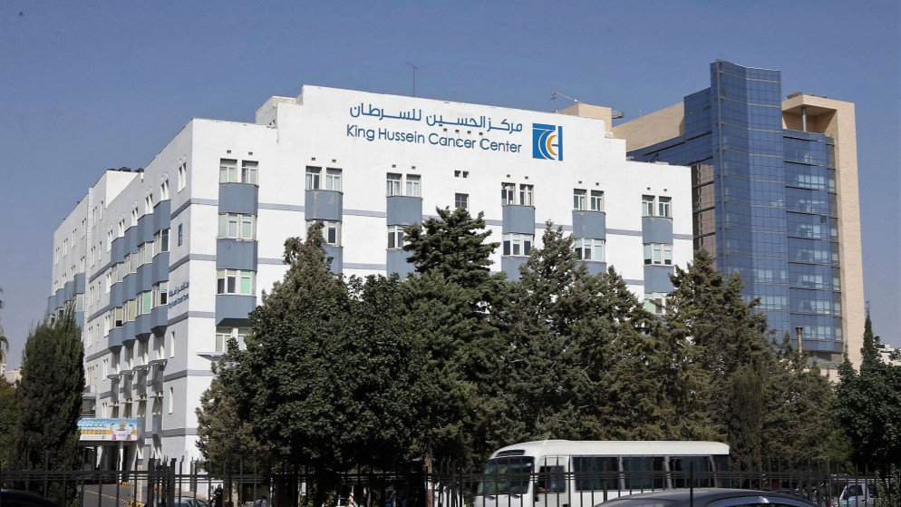 image - Center News Network White King Hussein Cancer Center building with blue accents, trees in front, and a bus on the street nearby.