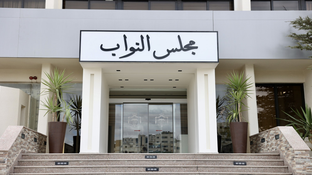 Entrance to a government building with a prominent Arabic sign reading مجلس النواب above glass doors, flanked by tall planters