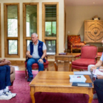 Five men sit in a cozy living room around a wooden coffee table, engaged in a discussion.