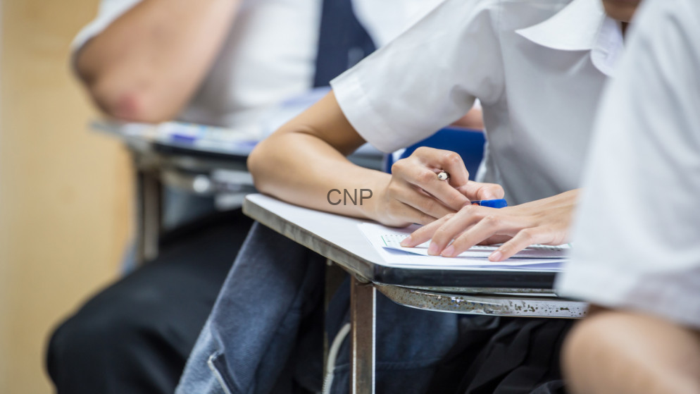 image - Center News Network Students in a classroom taking notes at desks, writing on papers with blue pens and notebooks visible in the foreground.