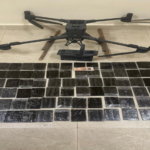 Quadcopter drone on a tiled floor with a grid of small black solar panels laid out in front of it.