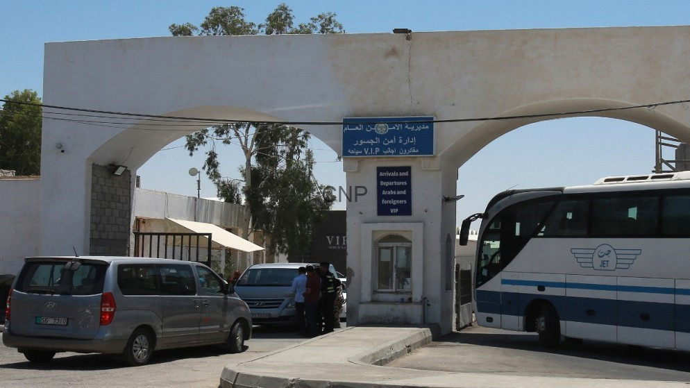 image - Center News Network Border checkpoint entrance with a blue 'Arrivals and Departures' sign, a VIP desk, and a large bus on the right amid parked cars.