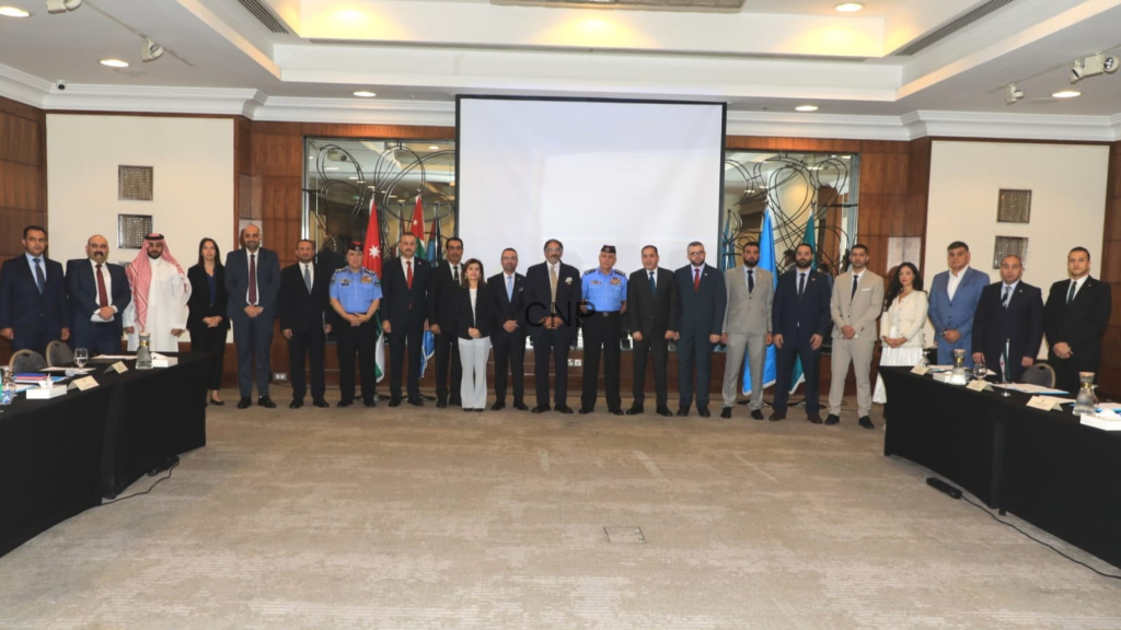 image - Center News Network Group of officials and delegates standing in a conference room with flags and a projector screen behind them, posing for a formal photo.