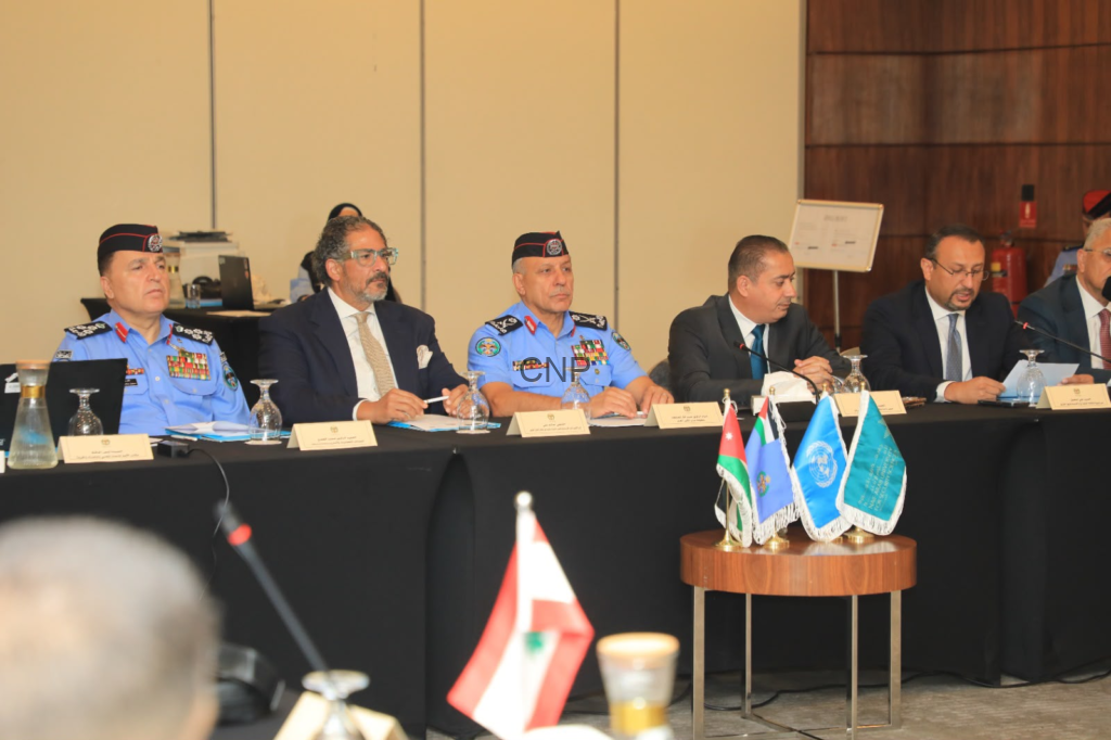 image - Center News Network Panel of officials seated at a long table during a formal conference; uniformed officers in blue dress with medals flank suited delegates, microphones and nameplates visible.