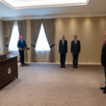 Formal briefing: speaker at an ornately carved podium with Jordan flags on the left; four men in suits observe.