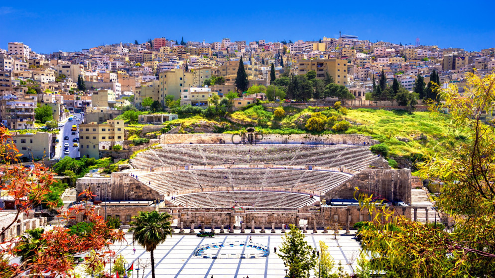 image - Center News Network Roman amphitheater in Amman, Jordan, with tiered stone seating against a hillside city under a bright blue sky.
