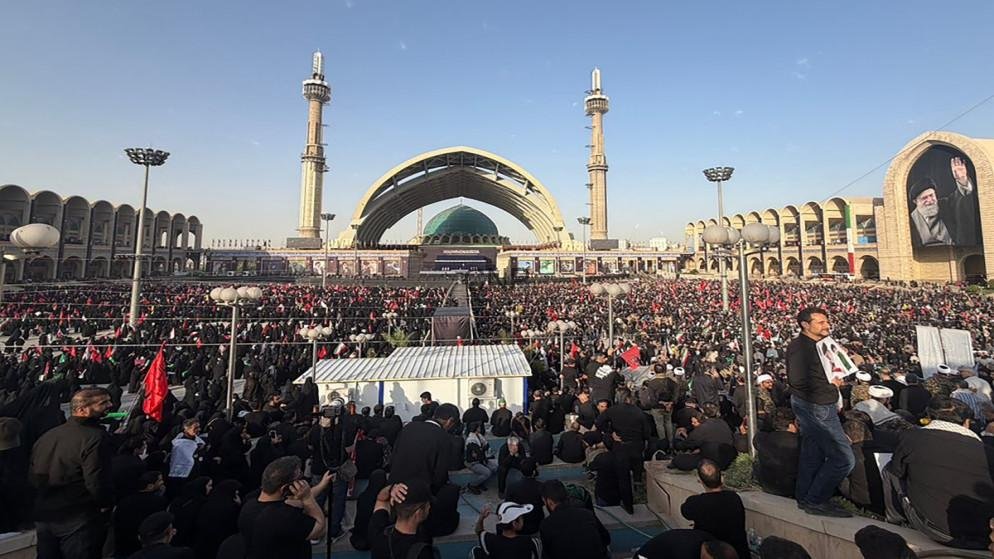 khamni - Center News Network Large crowd gathered at a mosque plaza with a green-domed shrine and tall minarets during a religious event.