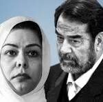 Two adults pose seriously against a blue backdrop; woman wearing a white headscarf and a man with dark hair and stubble.